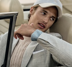 A man wearing a white knitwear, a jacket and a cap in a car.