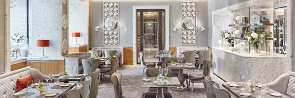 A view of the restaurant space at the Collins Room at The Berkeley with tables, chairs, the bar, and a view onto the hotel entrance through the doors in the background.