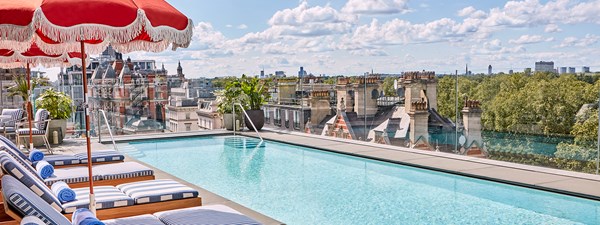 The rooftop pool and bar at The Berkeley with blue and white striped sun loungers, shaders and a view on Hyde Park and the London rooftops