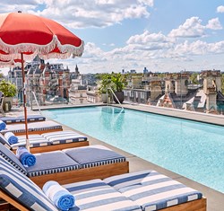 The rooftop pool and bar at The Berkeley with blue and white striped sun loungers, shaders and a view on Hyde Park and the London rooftops