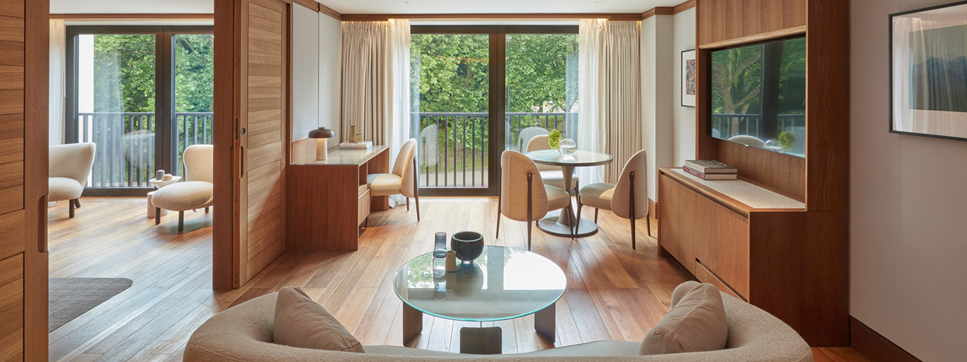 Park Suite at The Berkeley - view of the lounge with sofa and coffee table in the foreground, TV on the right, and office and dining table in the background with window view onto the park. Bedroom view on the left through open doors.